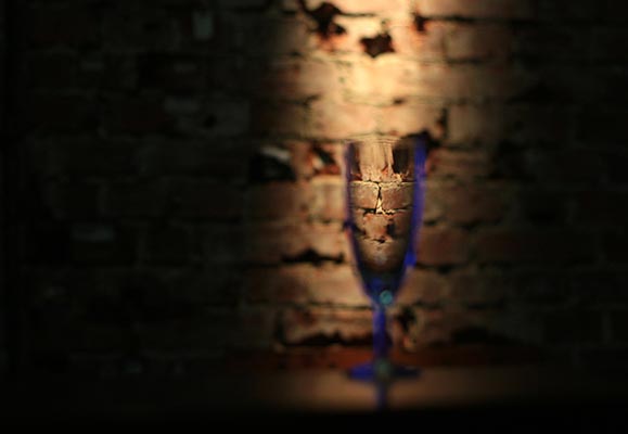 Sektglas vor einer Mauer, getaucht in Unschärfe. Fotografiert mit einem alten manuellen Objektiv.